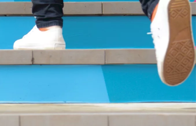 Image d'un escalier bleu et un étudiant qui marche dont on ne voit que les pieds