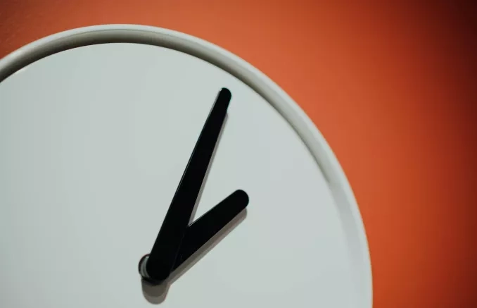Photo en gros plan sur les aiguilles d'une horloge blanche sur un fond orange
