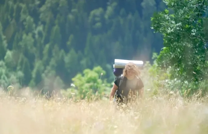 Photo d'un adolescent avec des cheveux blonds qui marche seul dans la nature. Il porte un sac à dos de randonnée.